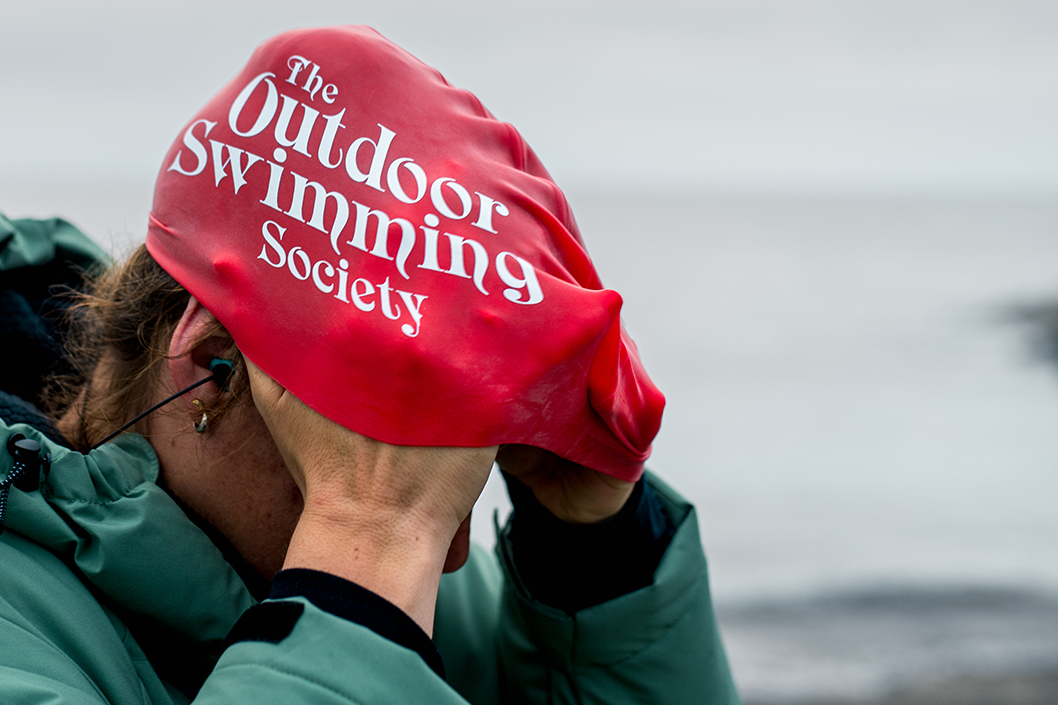 swimmer putting a red oss swim cap on their head