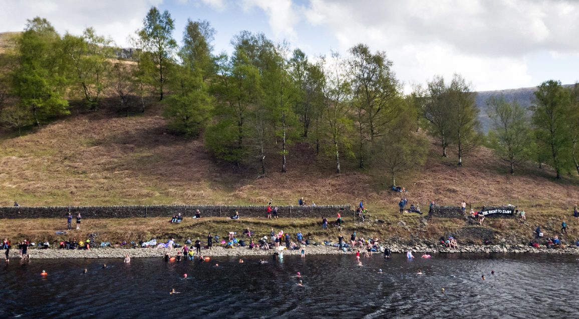 many swimmers on reservoir shore and water