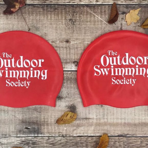 large and regular red swim hat with text The Outdoor Swimming Society written on it in white