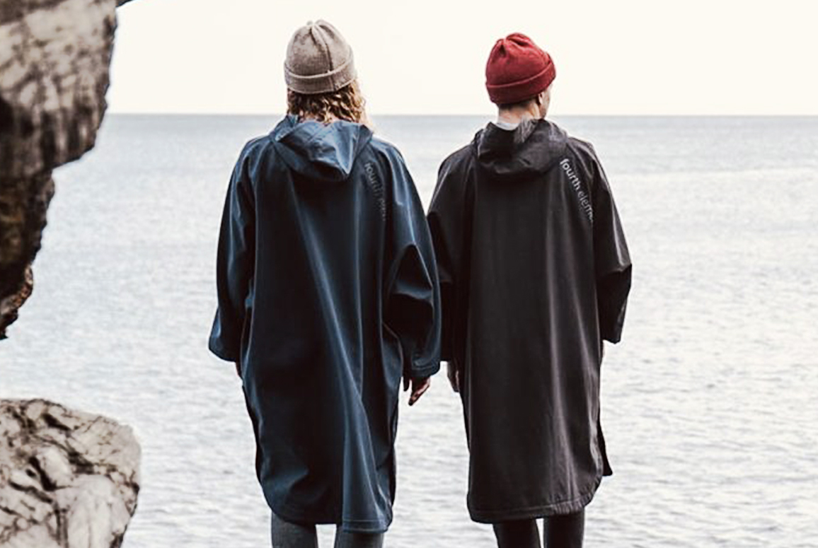 two people looking out to sea, one in a blue and one in a black storm poncho