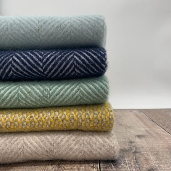 stack of blankets in duck egg blue, navy, sea green, yellow/grey, and hazel