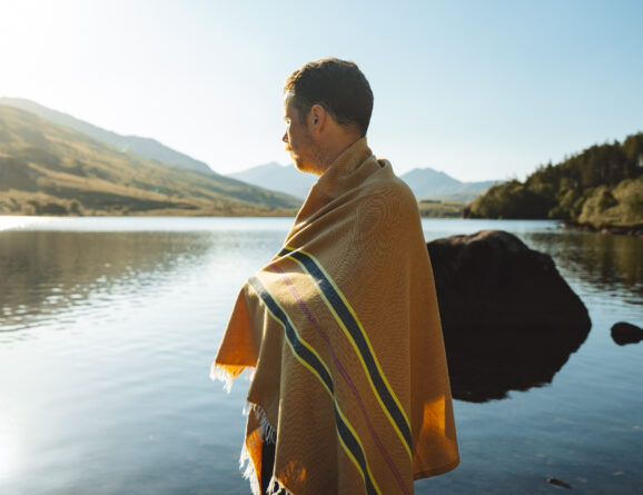Man wrapped in an OSS striped hammam towel, standing by a lake