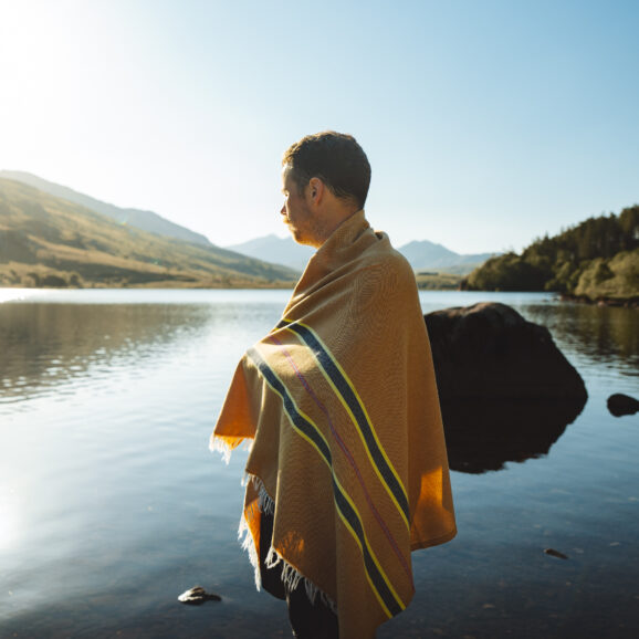 Man wrapped in an OSS striped hammam towel, standing by a lake