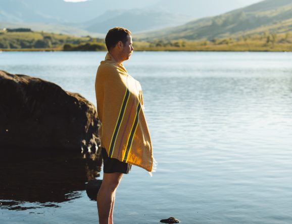 Man wrapped in an OSS striped hammam towel, standing by a lake