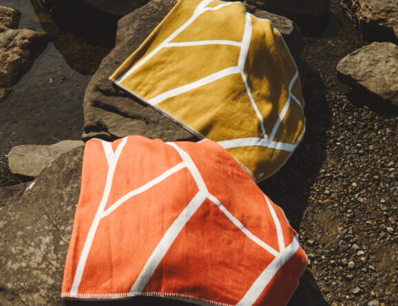 Burnt orange and golden blankets laid over rocks on the shoreline